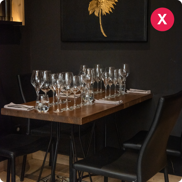 Une table faiblement éclairée avec des rangées de verres à vin vides et des serviettes pliées, évoquant une expérience de dégustation.