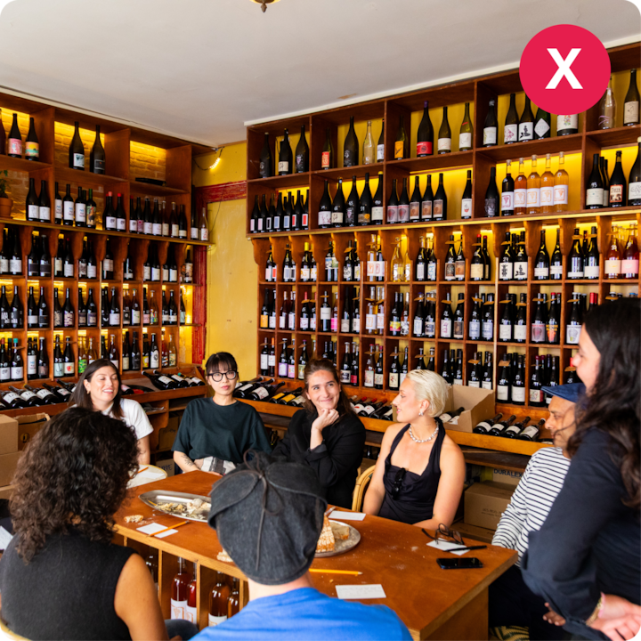 Intérieur d'une boutique de vin à l'éclairage chaleureux et aux étagères bordées de bouteilles de vin assorties, où un groupe de personnes est assis à une table pour une dégustation.
