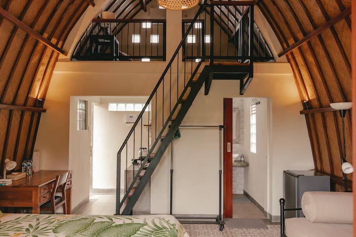 Interior of a cozy two-level wooden loft in Bali with a staircase leading to an upper floor, featuring tropical decor and warm lighting.