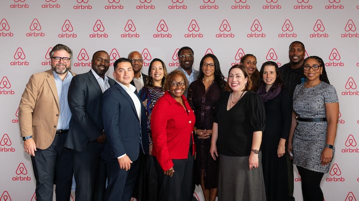 A diverse group of attendees posing for a photo in front of an Airbnb-branded step-and-repeat banner at an event.