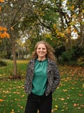 Helen standing outside on a green lawn with autumn trees