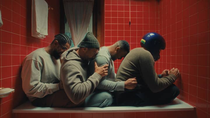 A stylized shot of the four-man Brazilian bobsled team in matching grey sweatsuits in a red-tiled bathtub at an Airbnb.