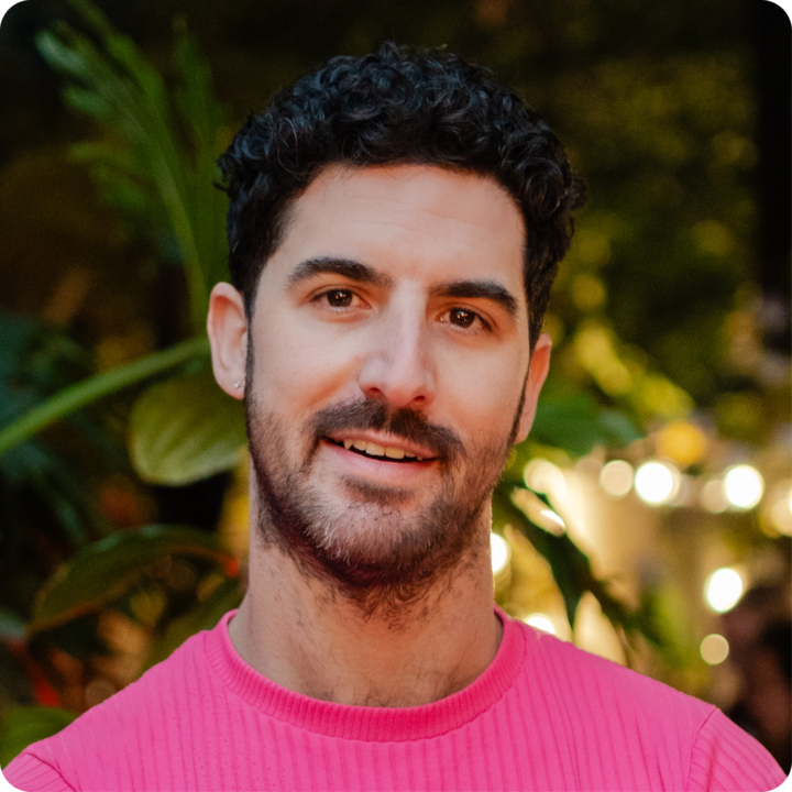 Portrait dans des conditions de faible luminosité mettant en scène une personne vêtue d'un t-shirt rose, avec une végétation luxuriante et des lumières vives en arrière-plan.