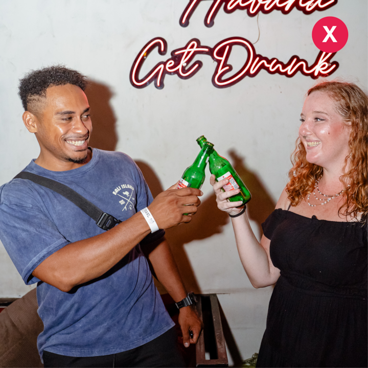 Deux personnes trinquent avec des bouteilles de bière vertes devant une enseigne lumineuse indiquant « How To Get Drunk » (Comment se saouler), avec une icône « X » rouge indiquant ce qu'il faut éviter.