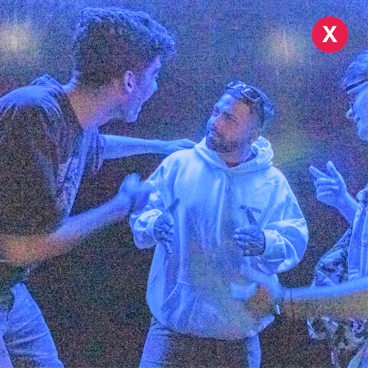 L'image montre un groupe de personnes dans un lieu sombre avec un éclairage inégal et une dominante bleue prononcée. Elle est marquée d'un « X » pour mettre en évidence les problèmes de luminosité.