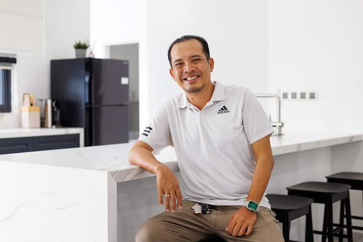 A person seated at a modern kitchen counter with white marble countertops and black stools, highlighting a clean and minimalist interior design.