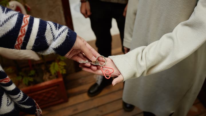 Close-up of one person handing house keys with a red heart-shaped keychain to another person, symbolizing tourism dispersal in regional areas.