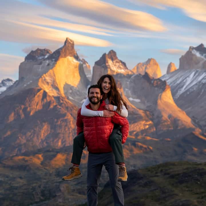 Picture of a man giving a woman a piggy back ride in front of a mountain range. They are both smiling. 