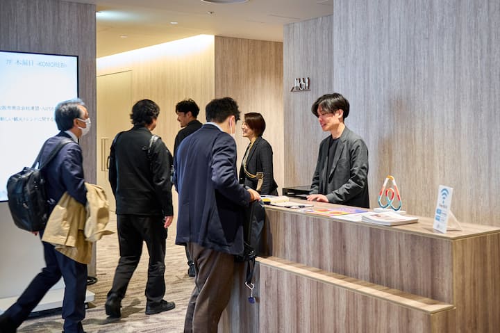 A modern office space featuring a reception desk with the Airbnb logo and informational materials. Several individuals are gathered near the counter, interacting professionally.