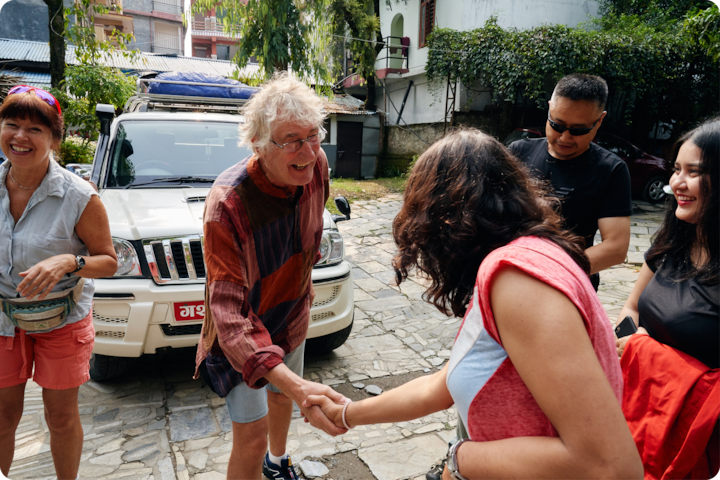 Deux personnes se serrent la main près d'un SUV blanc sur une allée pavée, avec d'autres personnes à proximité dans un cadre extérieur décontracté.