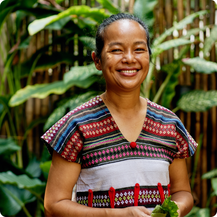 Une scène en plein air animée montrant une personne vêtue d'une tenue traditionnelle entourée de plantes tropicales et d'une clôture en bambou.