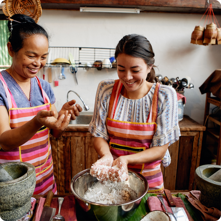 Des personnes en tabliers collaborent à la préparation d'un ingrédient dans un bol, entourées d'ustensiles dans une cuisine chaleureuse et accueillante.