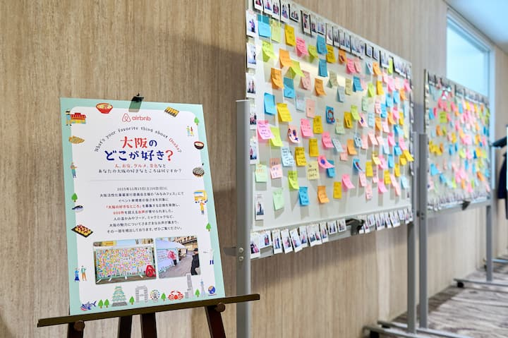 A board filled with colorful sticky notes and photos showcasing public opinions and favorite things about Osaka, alongside an Airbnb-branded informational poster inviting participation in a community campaign about Osaka.