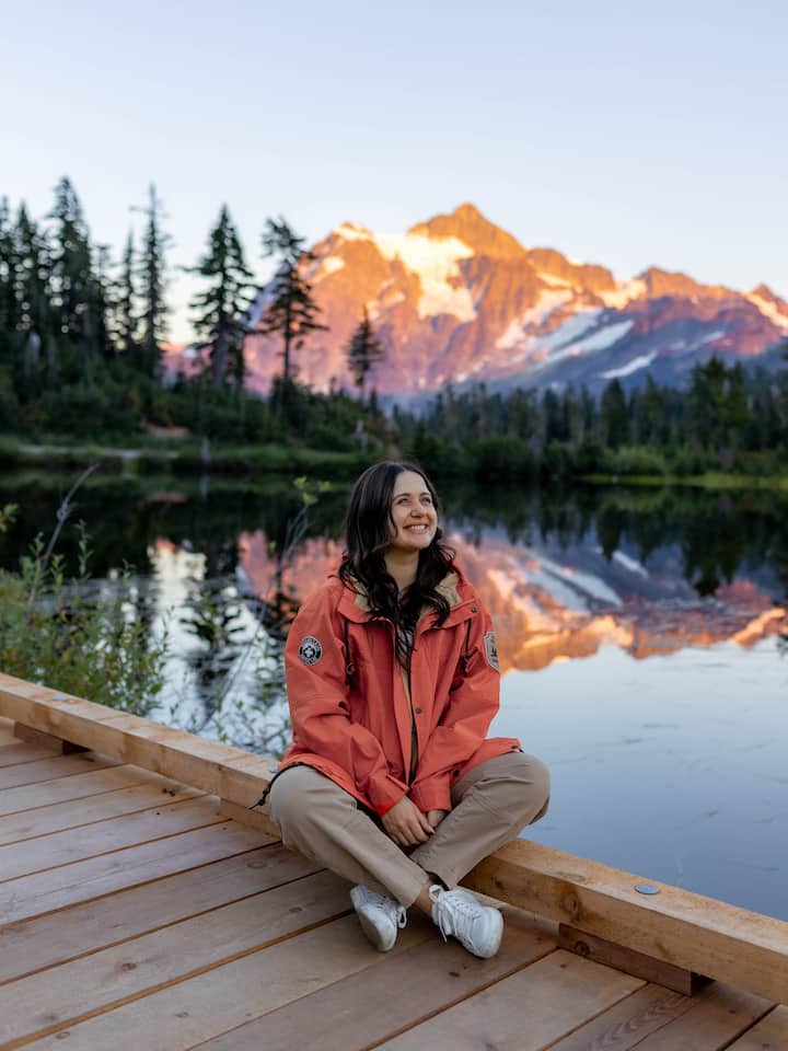 Veronika sitting on a dock smiling with a mountain and lake behind her