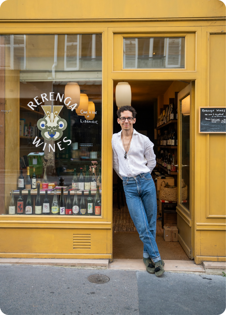 L'extérieur de « Rerenga Wines », un caviste à la façade jaune vif, avec une vitrine remplie de bouteilles de vin. La porte est ouverte, révélant un intérieur convivial avec des casiers à vin et une lumière douce.