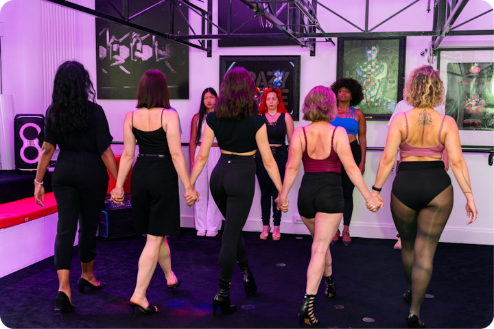 Des femmes dans un studio marchent main dans la main, dos à l'objectif, dans le cadre d'un exercice. Elles sont entourées d'œuvres d'art et de matériel de sport.