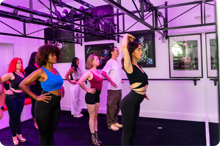 Un cours de danse dans un studio où les participants adoptent diverses poses, éclairés par des lumières violettes et entourés d'affiches artistiques.