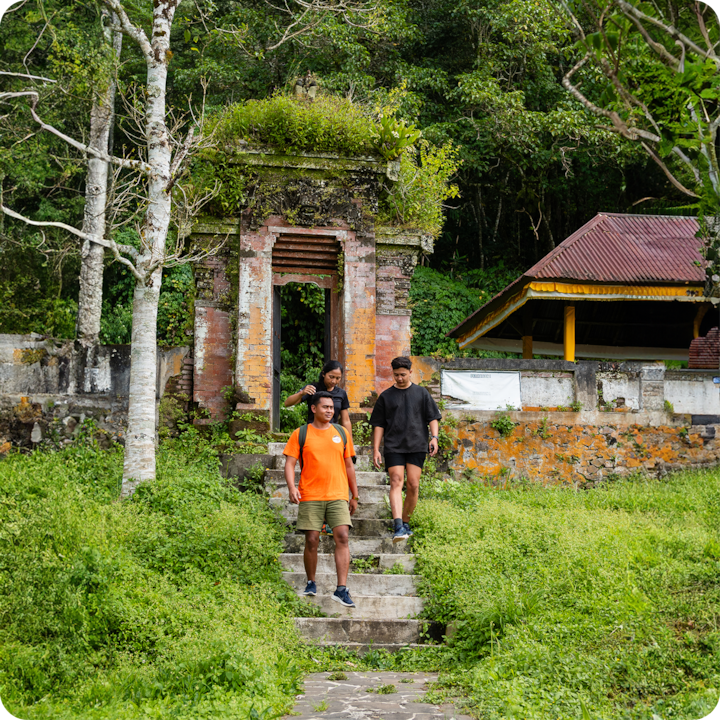 Un groupe explore un environnement extérieur à la végétation luxuriante, passant devant une arche en brique recouverte de mousse et une structure rurale traditionnelle.