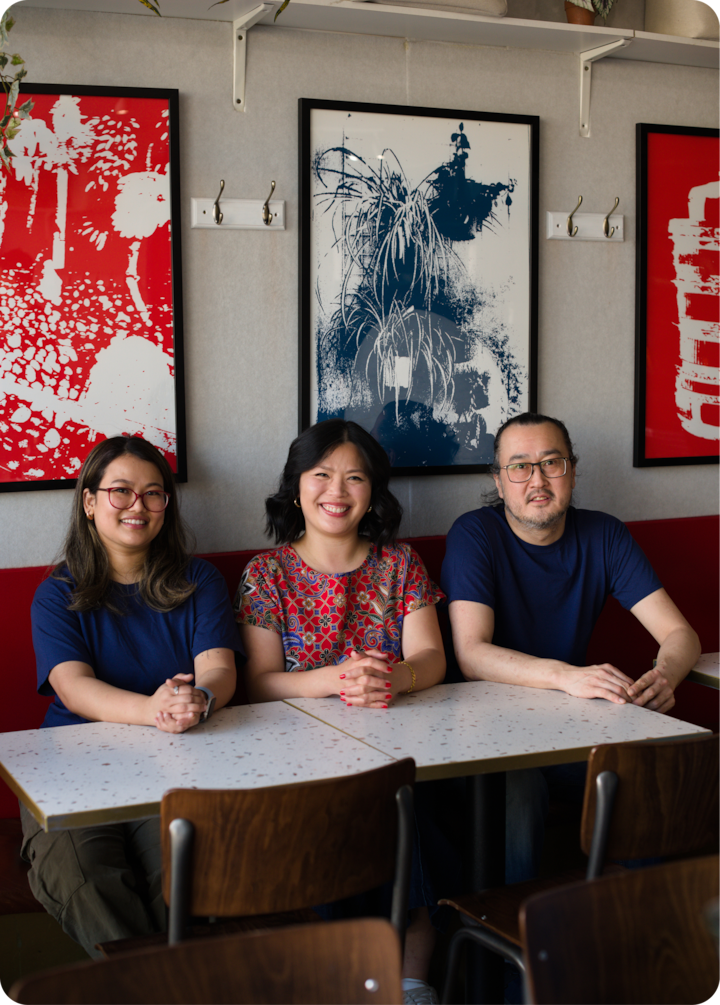 Trois personnes sont assises à une table dans un café au décor moderne, avec des œuvres d'art abstrait aux teintes vives de rouge et de bleu sur les murs et des chaises en bois autour de la table.
