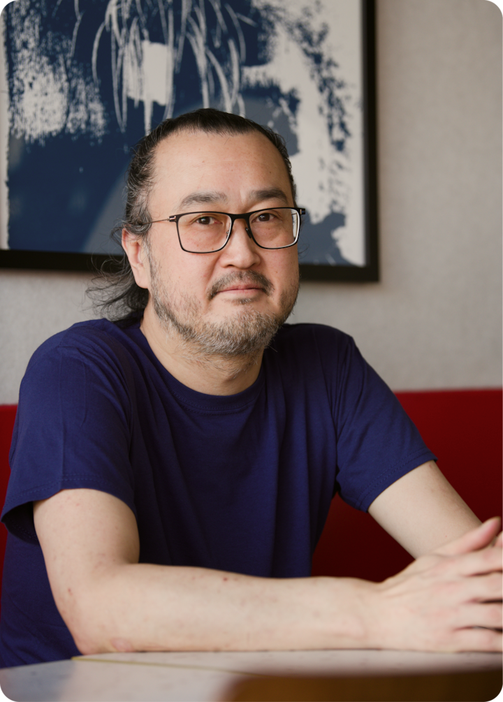 Une œuvre d'art abstraite bleu marine et blanche est accrochée au mur derrière une personne portant une chemise bleu foncé, assise à une table.