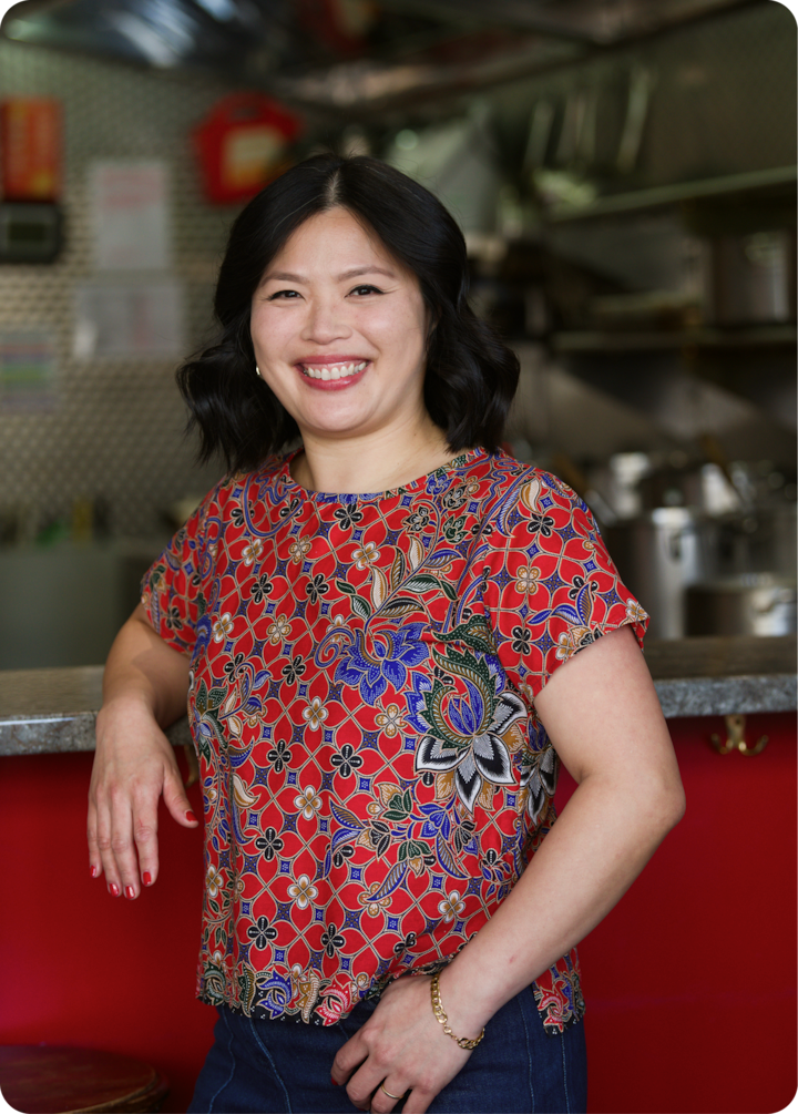 Une personne portant un haut rouge à fleurs se tient dans une cuisine aux surfaces et ustensiles métalliques, créant une atmosphère chaleureuse et accueillante.