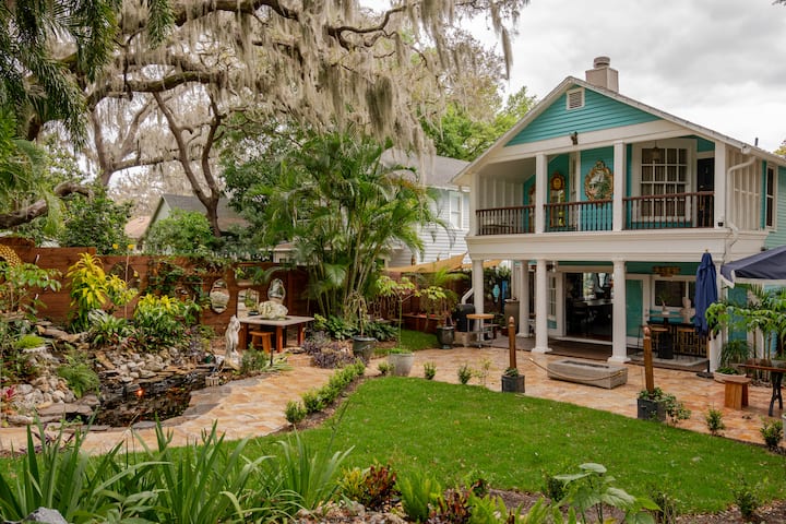 Une cour pittoresque avec une maison turquoise à deux étages, un jardin paysager, un bassin de carpes koï et de la mousse espagnole suspendue aux arbres.