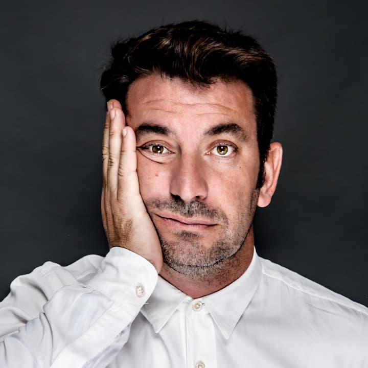 Arturo Valls, vestido con una camisa blanca, aparece en la imagen sobre un fondo oscuro con una mano tapándose parte de la cara.