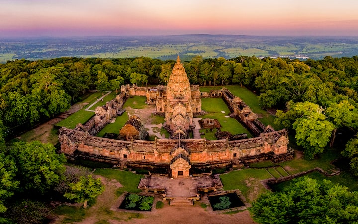 Aerial view of Phanom Rung Historical Park in Buriram, Thailand, featuring ancient Khmer architecture surrounded by lush greenery during sunset.