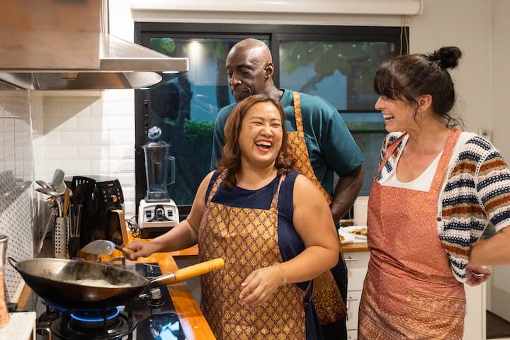 Three people wearing aprons cooking together in a kitchen, illustrating a communal and cultural experience available through Airbnb stays.