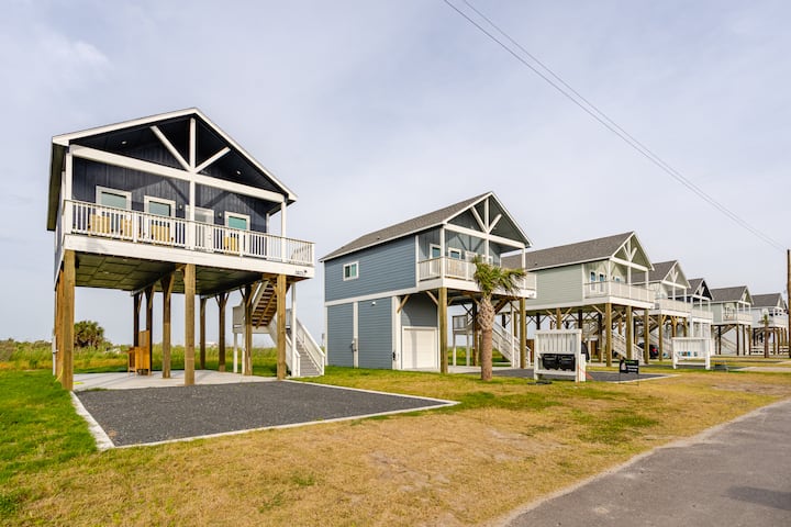 Une rangée de maisons de vacances construites sur pilotis avec balcons, près d'une grande plaine dans une rue calme.