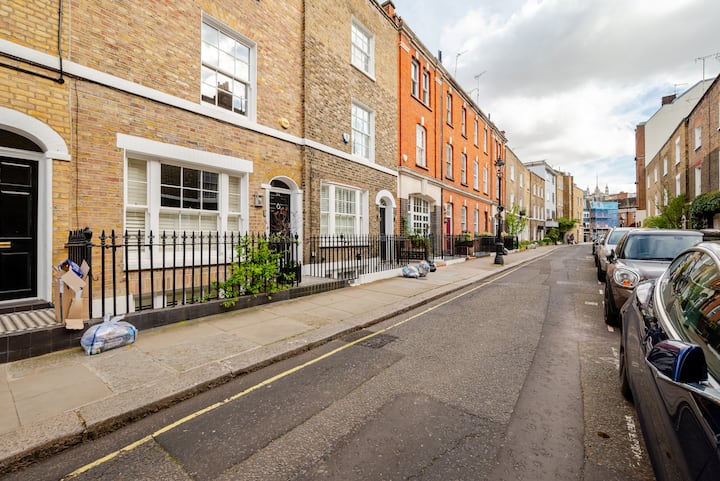 Vue d'une rue résidentielle avec des maisons de ville aux couleurs vives en briques rouge vif, orange et beige, dans un mélange de styles architecturaux.