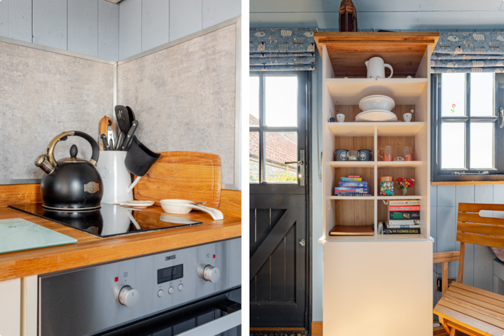 Une scène de cuisine rustique montrant une plaque de cuisson avec des ustensiles de cuisine et une armoire contenant des assiettes, des livres et des objets décoratifs, placée à côté d'une porte et d'une fenêtre laissant entrer la lumière naturelle.