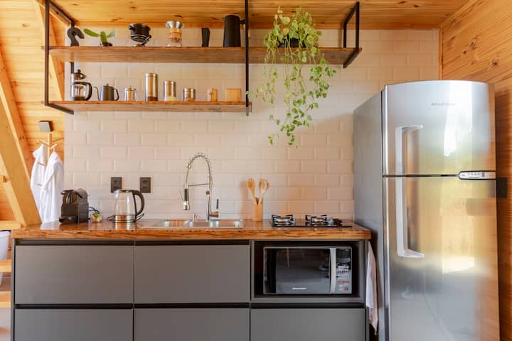 Un espace cuisine accueillant avec des accents en bois, un réfrigérateur en acier inoxydable, un évier moderne et des étagères ouvertes contenant des plantes, des ustensiles de cuisine et des accessoires.