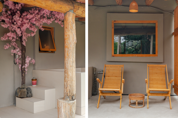 Un espace couvert paisible avec un cerisier en fleurs décoratif et quelques marches près de poutres en bois rustiques. Plus loin se trouvent deux chaises longues en bois, une petite table et une fenêtre reflétant la verdure environnante.