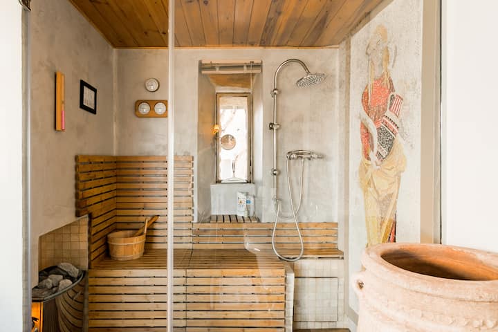 Un sauna élégant de style spa avec des sièges en bois, une douche, des mosaïques décoratives et une lumière d'ambiance chaleureuse.