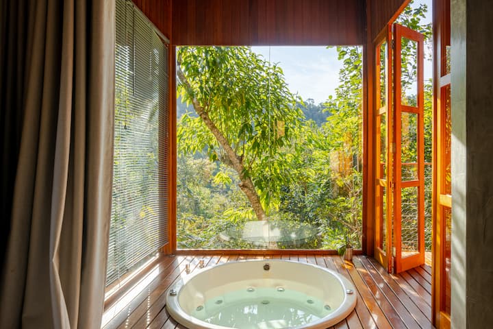 Un jacuzzi intérieur luxueux avec vue sur la forêt, entouré de grandes baies vitrées et de portes en bois ouvertes, pour un séjour paisible.