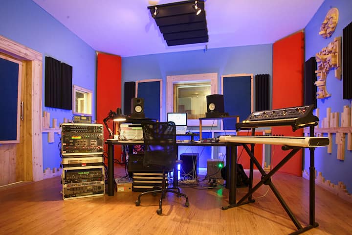 Studio de musique de luxe doté d'un équipement audio professionnel, de murs insonorisés et d'un décor moderne dans un espace bleu et rouge vif.