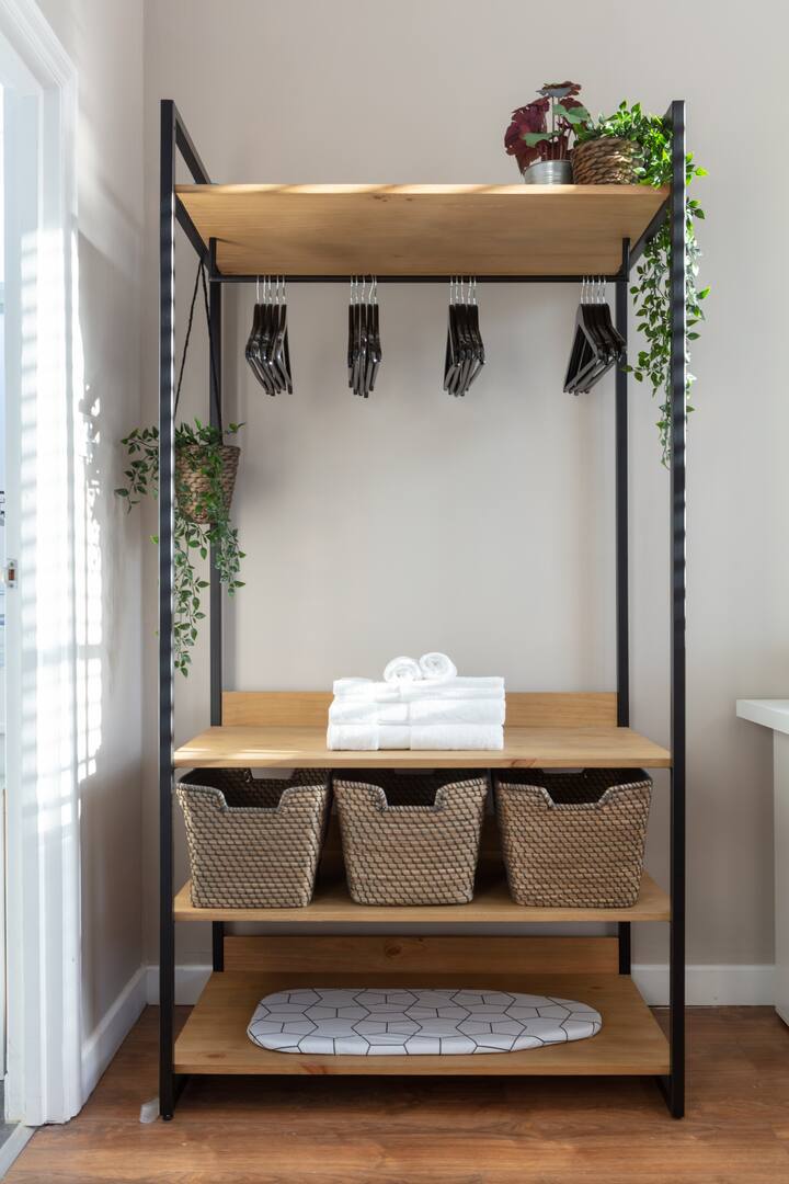 Un espace de rangement au design moderne et minimaliste avec des cintres noirs, des serviettes pliées, des paniers tressés et des plantes vertes.