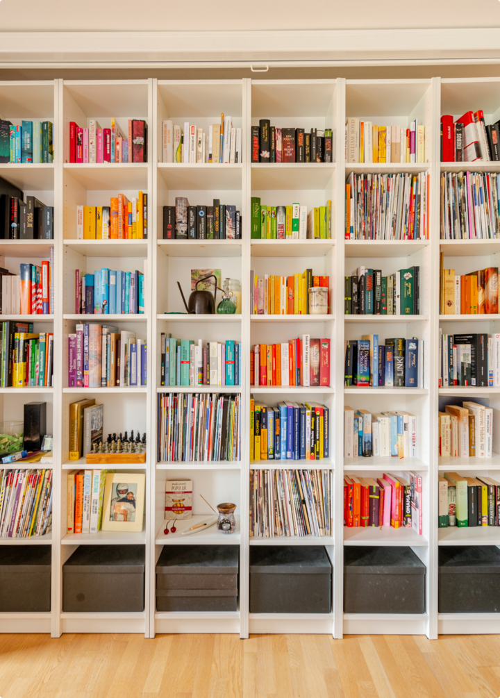 Une bibliothèque lumineuse avec des livres, des magazines et des objets décoratifs bien rangés, mettant en valeur un espace de lecture coloré et accueillant.