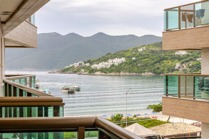 Vue depuis un balcon doté de garde-fous modernes en verre donnant sur des eaux calmes, des collines verdoyantes avec des maisons blanches et des bateaux amarrés.