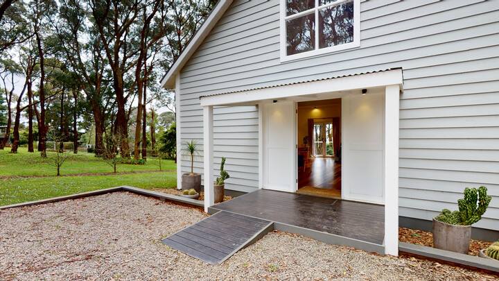 Plan rapproché de l'entrée d'une maison avec une rampe d'accès en bois, mettant en avant les équipements inclusifs dans un cadre naturel.