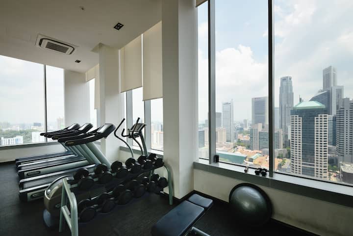 Une salle de sport équipée de matériel d'entraînement, notamment des tapis de course et des haltères, offrant une vue panoramique sur des gratte-ciels à travers des baies vitrées.