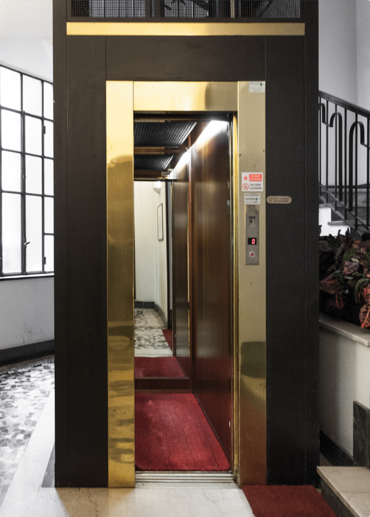 Un ascenseur avec des portes dorées réfléchissantes, un tapis rouge à l'intérieur et des escaliers adjacents, mettant en valeur les équipements de l'espace partagé.