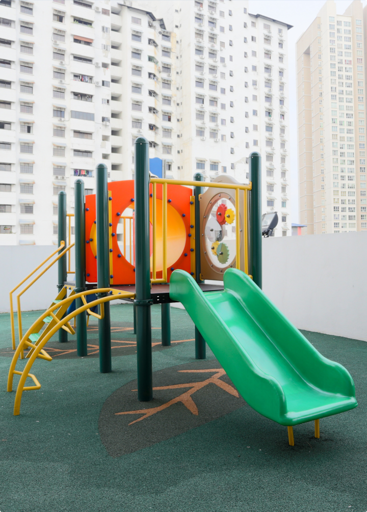 Une aire de jeux pour enfants avec un toboggan vert et des équipements de jeu colorés, entourée de grands immeubles d'habitation.