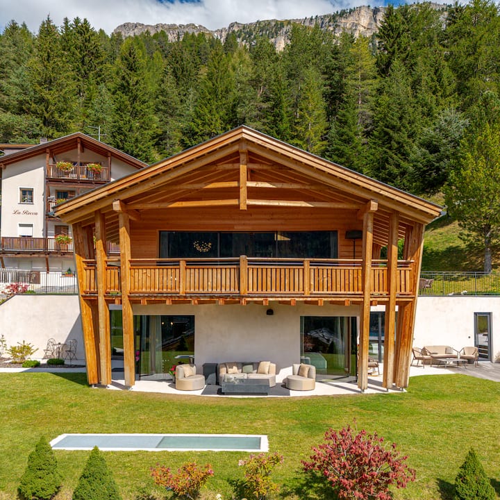 Un logement de style cabane en bois doté d'un grand balcon, d'un salon d'extérieur et d'une pelouse. Il est entouré d'arbres et de montagnes, le tout dans un cadre pittoresque.