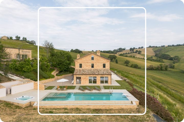 Vue aérienne d'une villa de campagne dotée d'une piscine et de sièges sur la terrasse. La vue panoramique donne sur de vastes terres agricoles et de la végétation.