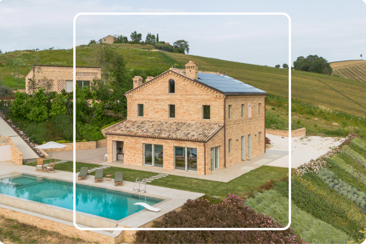 Une vue en hauteur d'un logement spacieux, avec des murs en briques de terre cuite et des sièges au bord de la piscine. Cette propriété se trouve au cœur d'un espace vert bien entretenu et de vastes terres agricoles.