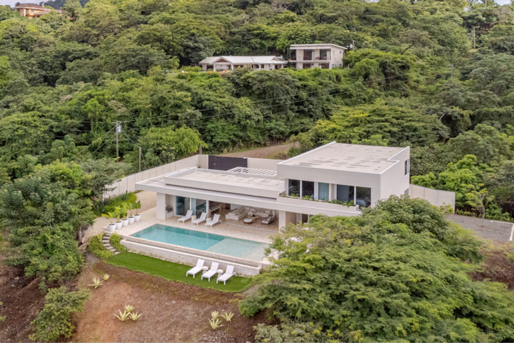 Une maison moderne et élégante avec une grande piscine, un espace de détente extérieur et une forêt tropicale dense tout autour.