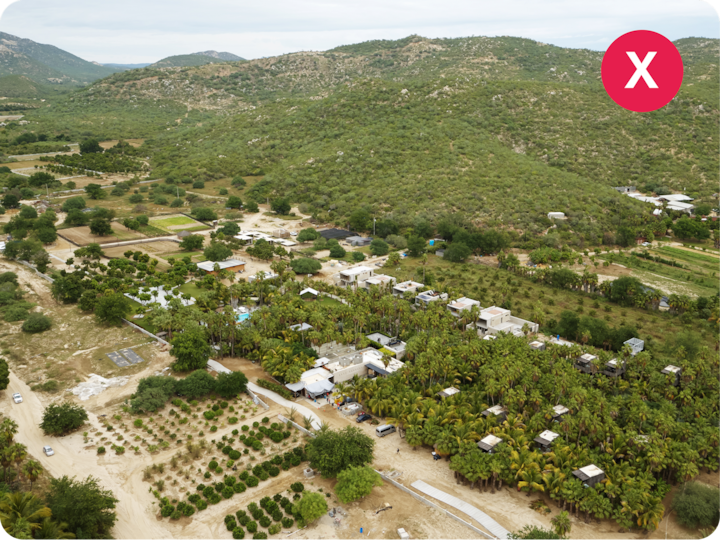 Cliché réalisé par drone représentant un quartier résidentiel au cœur d'une végétation luxuriante, notamment des palmiers et des terres agricoles. Les collines vallonnées en arrière-plan complètent ce paysage.