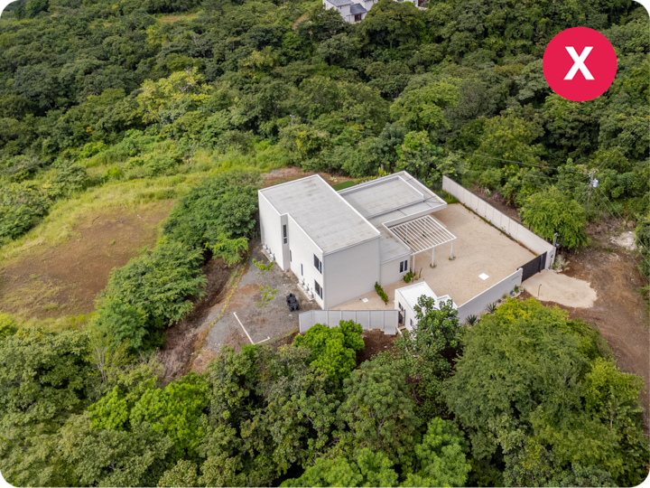 Vue aérienne d'une maison moderne et épurée. Elle se trouve au cœur d'une végétation luxuriante et est dotée d'un patio extérieur.